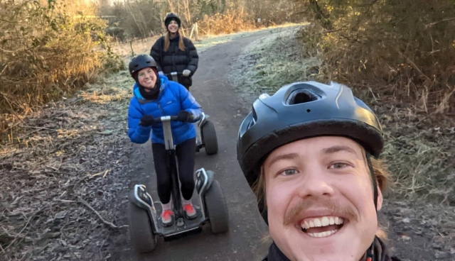  Tres amigos con cascos azules dando vueltas en segway por el parque y sonriendo 