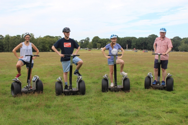  Familia de cuatro personas con cascos azules posando, sonriendo y divirtiéndose duranle su viaje en segway en el parque 