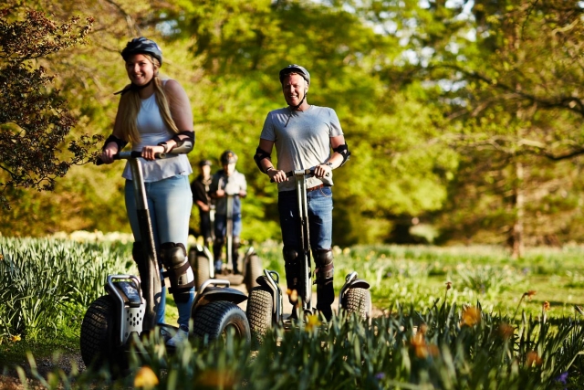 Dos parejas vestidas de negro cascos, sonriendo y divirtiéndose duranle su aventura en segway en el parque 