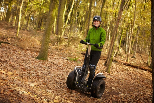 Mujer con suéter verde, casco negro, sonriendo y divirtiéndose duranle su sesión en segway en el parque 