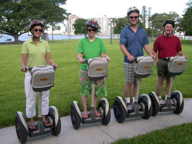  Dos mujes y dos hombres sonriendo, usando cascos negros duranle su sesión de segway