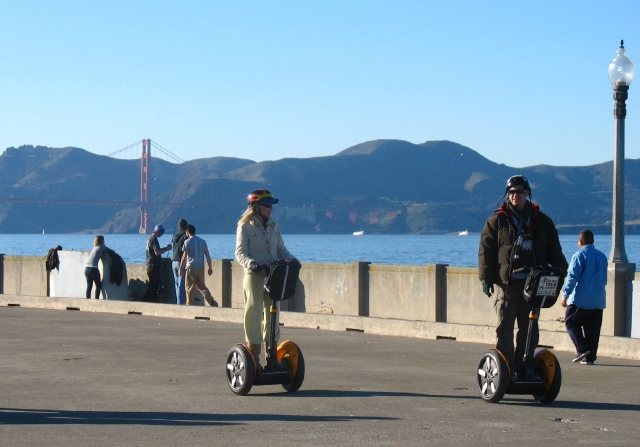  Niño y niña con cascos negros duranle su aventura en segway por el parque y el mar al fondo 