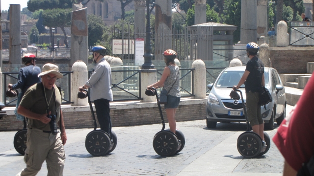 Hombre y dos mujes con cascos rojos y azules recorriendo en segway el parque y la ciudad 