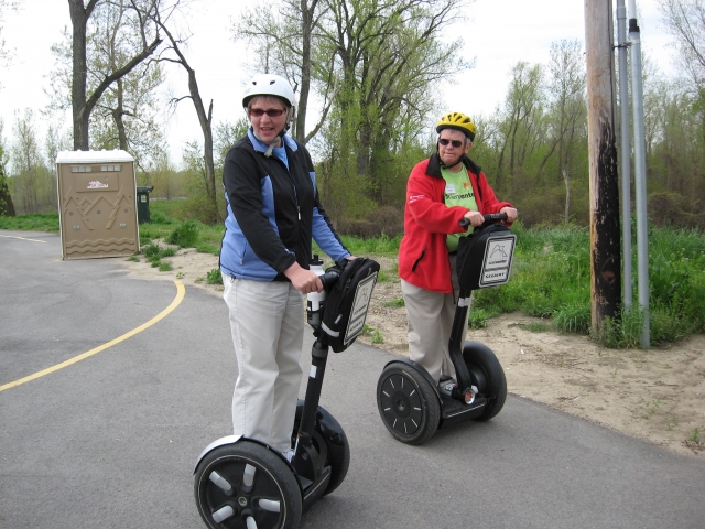  Hombre con casco blanco y chamarra azul y mujer con casco amarillo y chamarra roja dando un recorrido por el parque en segway 