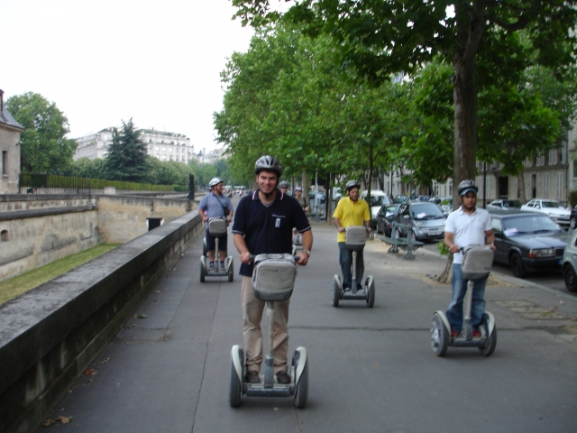 Grupo de personas sonriendo, con cascos azules y haciendo un recorrido en segway por el parque y la ciudad 