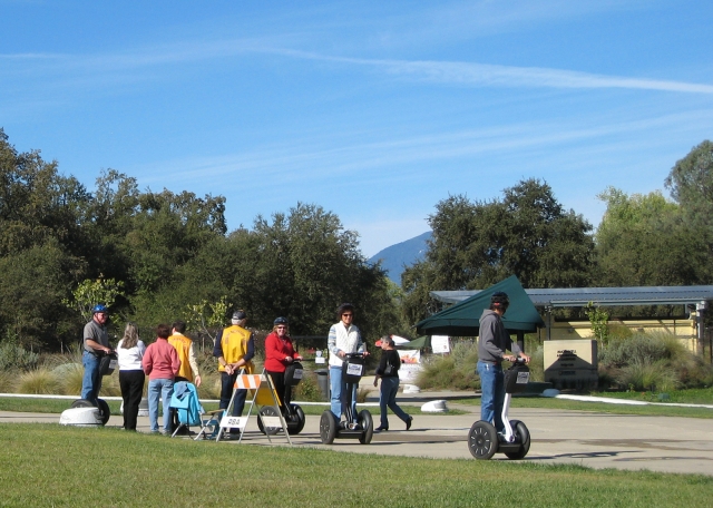  Grupo de personas con camisetas rojas, naranjas y amarillas duranle su aventura en segway en el parque y el lago 