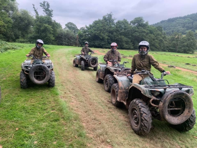  4 amigos vestidos con trajes de camuflaje y cascos negros en cuatrimotos.
