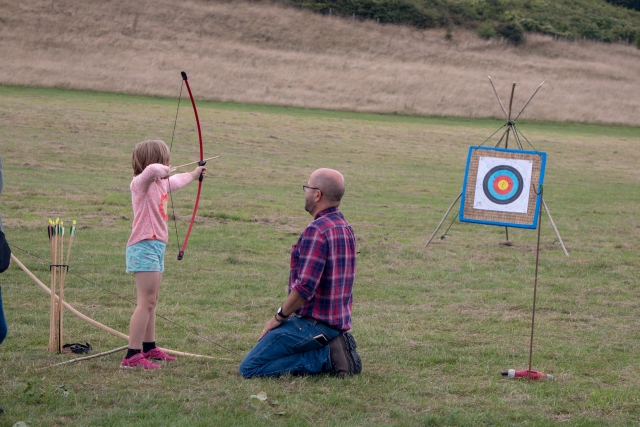 Niña con playera rosa y pantalones cortos azules haciendo jalo con arco con un instructor justo a su lado