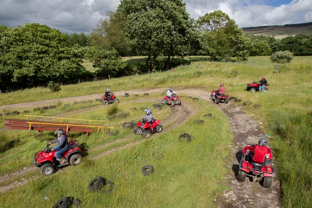  Aventureros con cascos y manejando cuatrimotos rojos por el bosque 