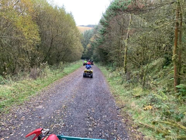  Chavos manejando cuatrimotos rojos por el bosque y usando cascos y monos de conducción 