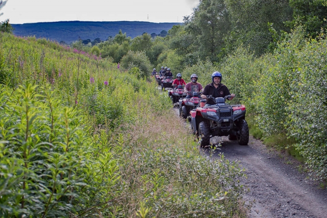 Instructor con casco azul y, detrás de él, un grupo de niños con casco y manejando cuatrimotos rojos por el bosque 