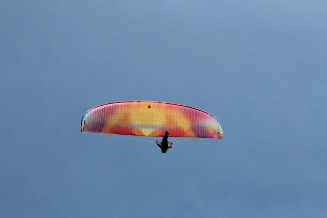  Aventurero con traje rojo sobrevolando con parapenle de colores 