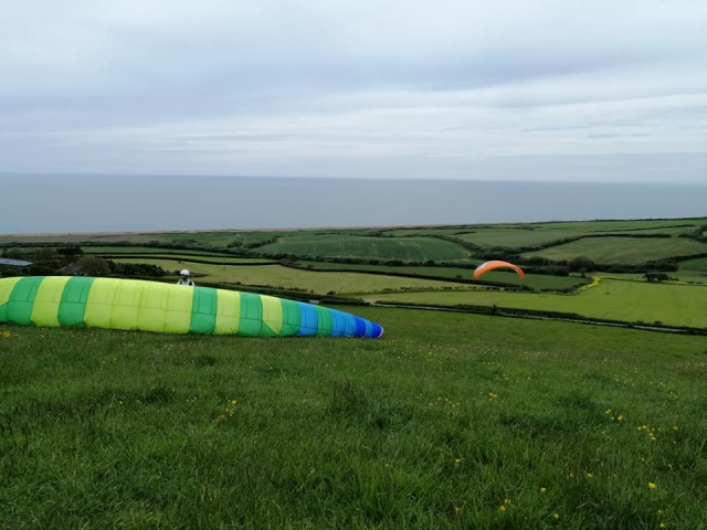 Dos personas con cascos blancos y preparándose para volar con parapentes naranja y verde 