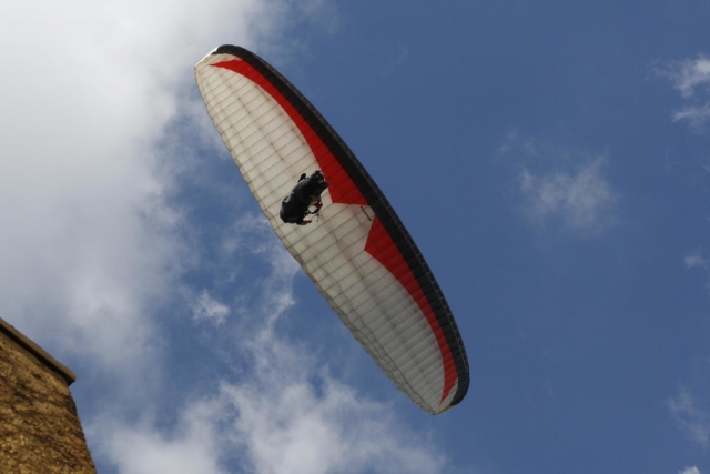  Persona volando sobre la costa, acantilado al fondo y usando parapenle blanco y rojo 