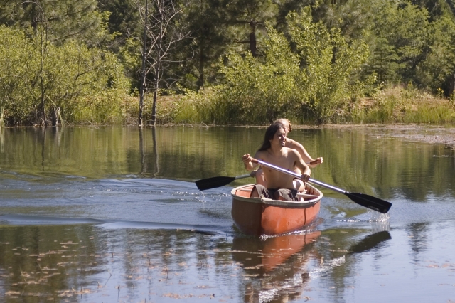Dos chicos sin camisa navegando en canoa por el río