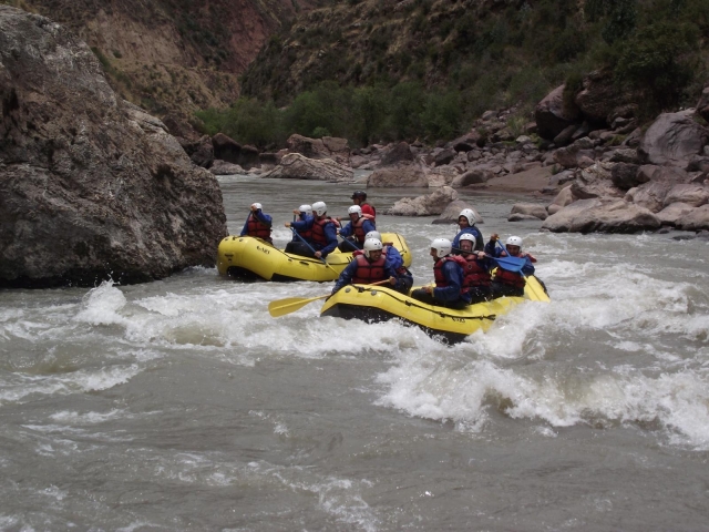 Dos grupos con cascos blancos, flotadores rojos y traje de neopreno azul haciendo rafting en un barco amarillo