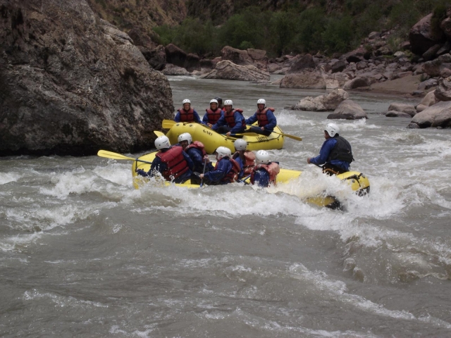Personas con casco blanco, flotadores rojos, traje de neopreno azul y rafting en un barco amarillo