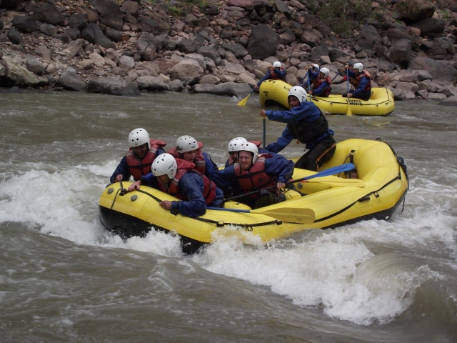 Dos grupos vistiendo flotadores rojos, trajes de neopreno azules y haciendo rafting por el río.