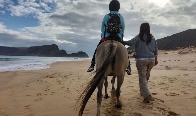 Una instructora acompaña a pie a una niña a lomos de un caballo