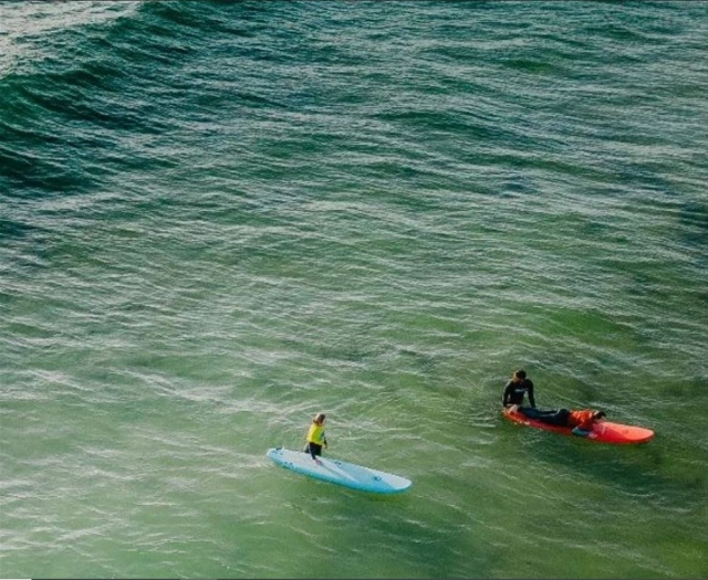 Dos surfistas con tablas de color azul y rojo adentrándose en el agua