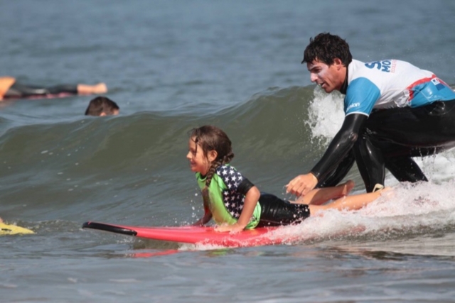 El instructor ayuda a su alumno a surfear la ola 